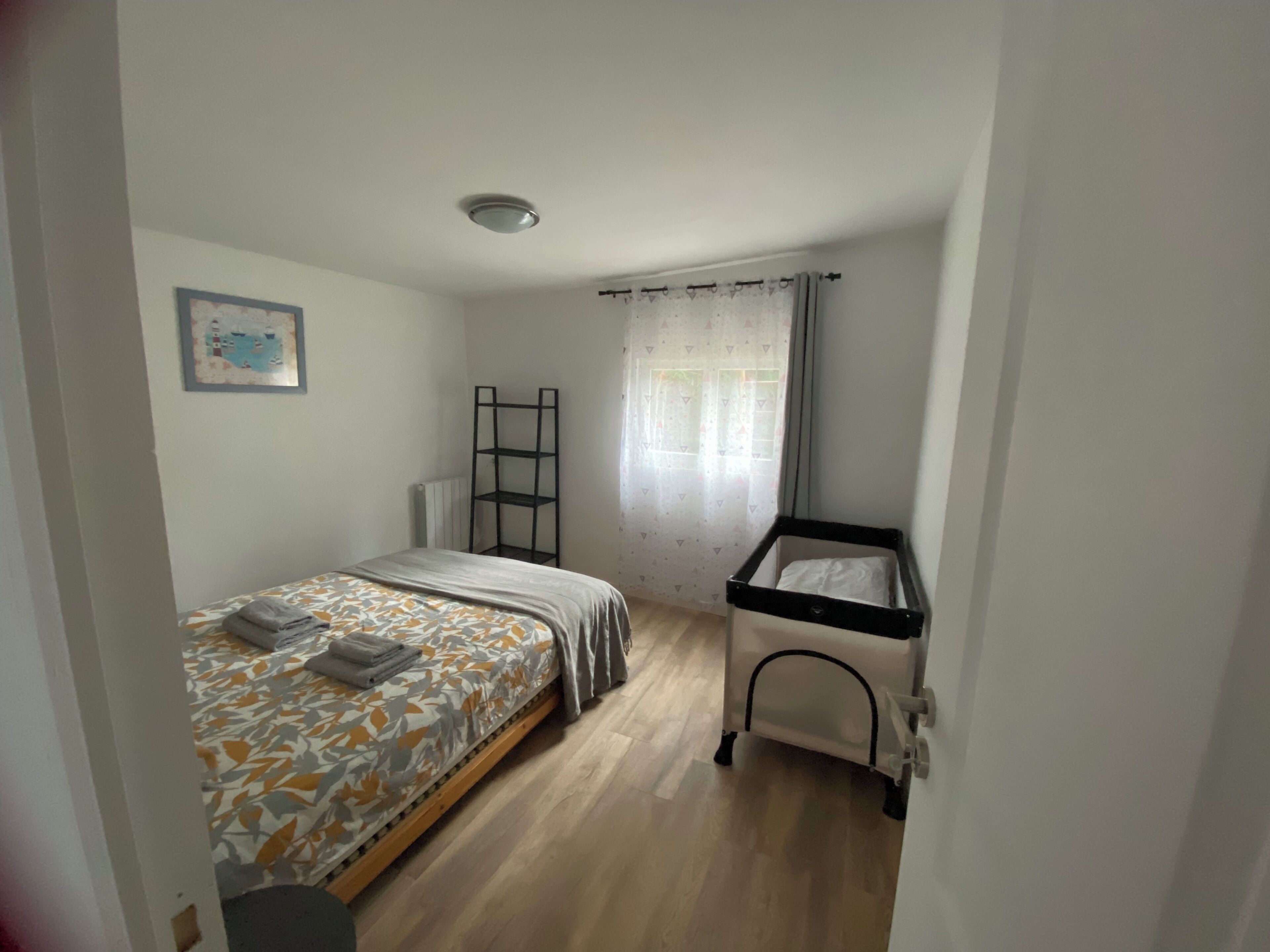 Une chambre à coucher avec un lit, un berceau, un radiateur et une fenêtre avec des rideaux.