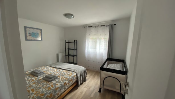 A bedroom with a bed, a crib, a radiator, and a window with curtains.