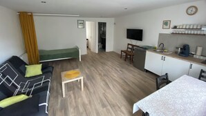 A compact living space with a sofa, a small table, a kitchenette, and a television.