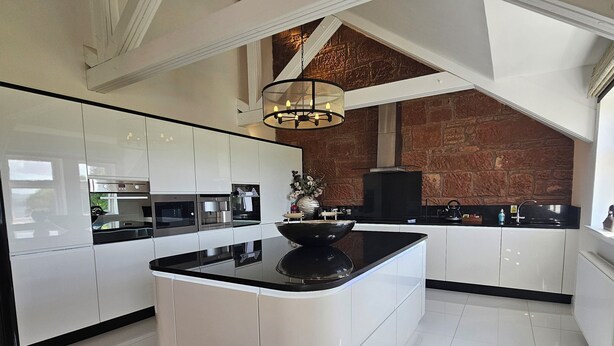 A modern kitchen with white cabinetry, a central island, and a stone accent wall.