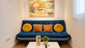 En blå sofa med to gule puder, et hvidt sofabord, en vase og en lille plante.