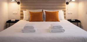 A neatly made bed with white linens and two folded towels in front, a headboard with a light wood finish, and two bedside tables with lamps and a phone. - Latina I (Madrid)