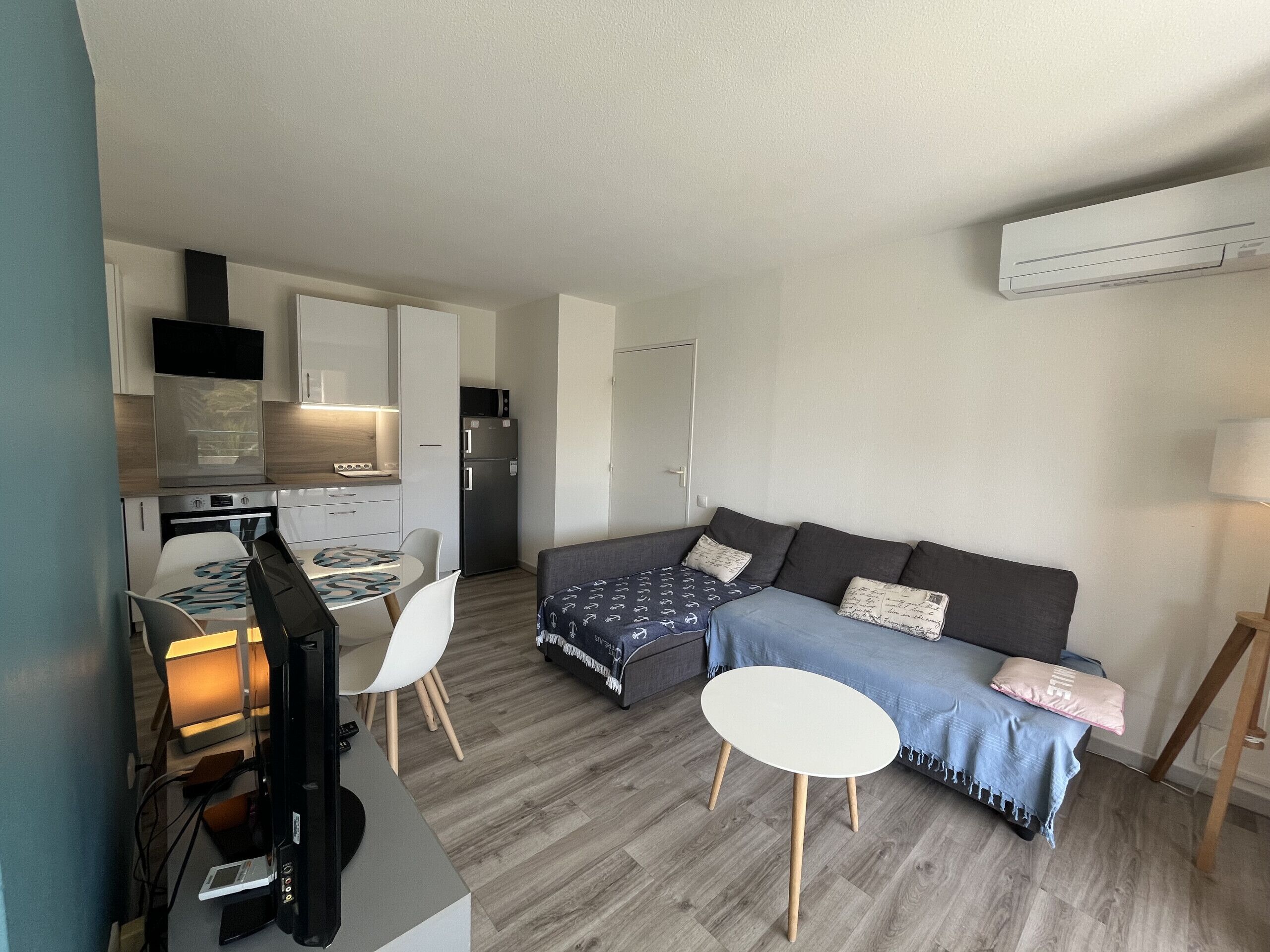 Un espacio habitable compacto con kitchenette, un sofá, una pequeña mesa redonda y un televisor.