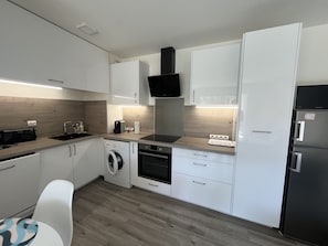 A compact kitchen with a washing machine, a built-in oven, and a refrigerator. - Cesaree Residence – Renovated 2-room apartment with pool view, air conditioning, garage and terrace – Sleeps 4. (Fréjus)