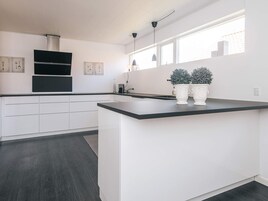 A modern kitchen with white cabinetry, a black countertop, and two potted plants.