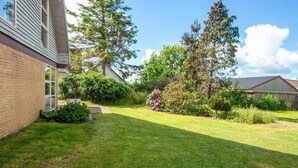 Un patio trasero residencial con césped, un árbol alto y una casa de ladrillo.