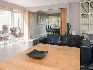 A modern living room with a wooden dining table, black leather sofa, and a cactus plant. - 8 Person Holiday Home in Hadsund (Hadsund)