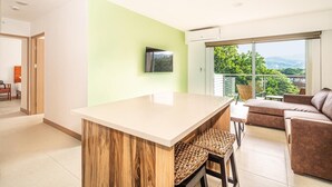 Un salon moderne avec une grande fenêtre, un canapé, une table basse et un téléviseur fixé au mur.