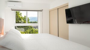Une chambre d’hôtel avec un lit, un téléviseur fixé au mur et une fenêtre donnant sur un paysage verdoyant et montagneux.