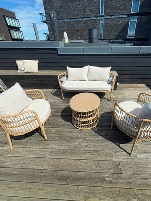 A rooftop patio with wicker furniture, including a sofa and chairs, and a round table.