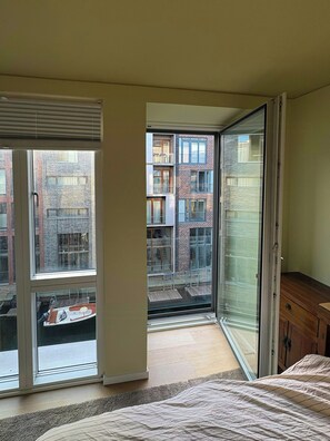 A bedroom with a large sliding glass door leading to a balcony, a wooden dresser, and a bed with a patterned bedspread.