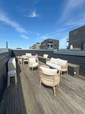 A rooftop deck with wicker furniture, a small table, and a white stool.