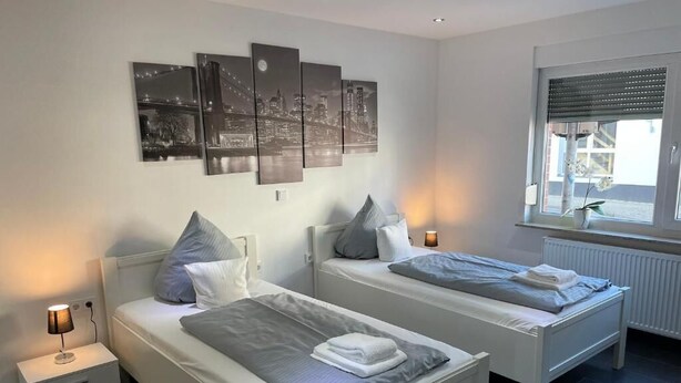 Une chambre avec deux lits, une table de chevet, une fenêtre avec des stores et des œuvres d’art murales.