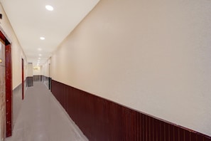 A long, narrow hallway with a wooden panel on one side and a plain wall on the other, leading to a door at the end.