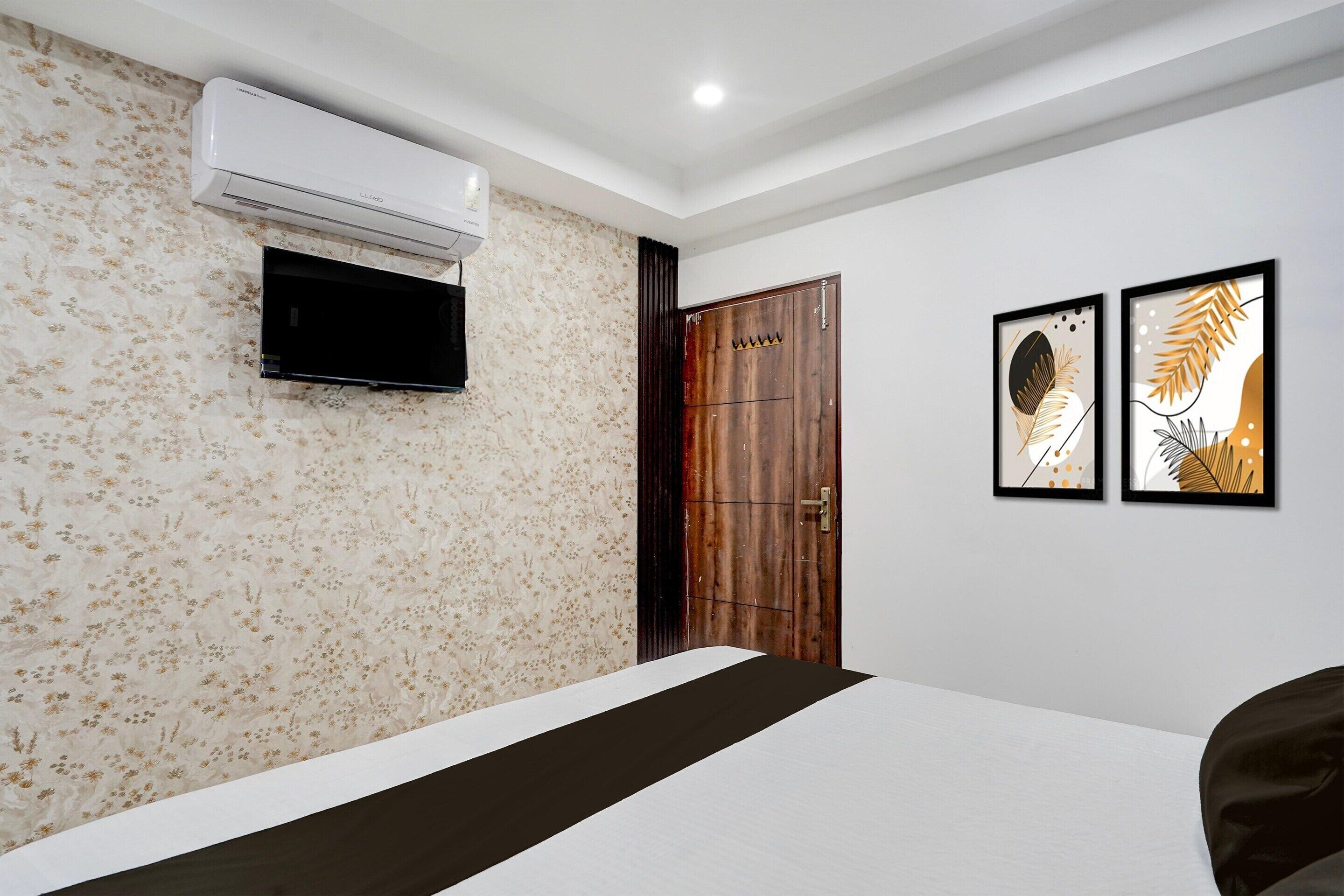 A hotel room with a bed, an air conditioning unit, a television, and two framed artworks on the wall.