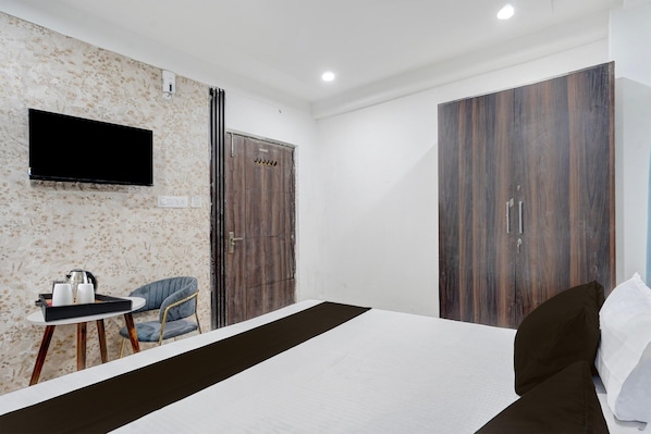 Una habitación de hotel con cama, televisor montado en la pared, armario y una pequeña mesa con silla.