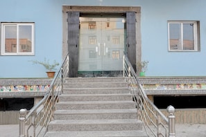 A set of stone steps leading to a building entrance with a metal railing, a tiled border, and a potted plant.