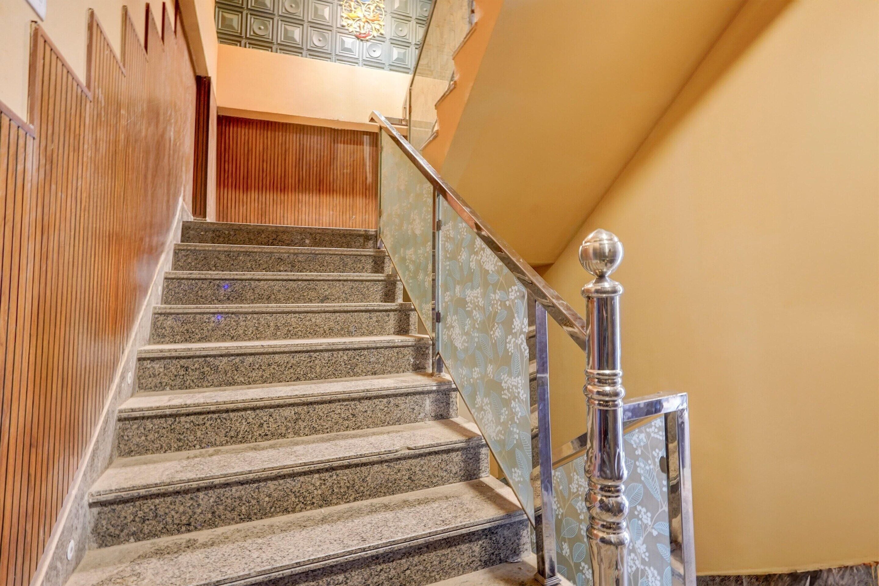 A staircase with granite steps, a wooden wall on one side, and a metal railing with a floral pattern on the other.