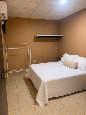 A hotel room with a bed, a towel rack, a heater, and a wall-mounted air conditioning unit.