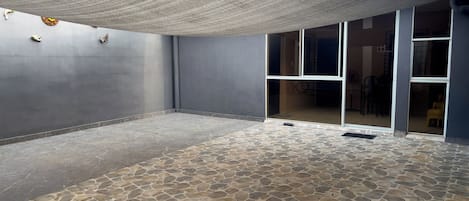 A covered outdoor area with stone flooring and a large sliding glass door leading to an interior space.