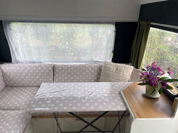 Un interior de caravana acogedor con un sofá seccional, una mesita y una ventana con vistas a la vegetación.