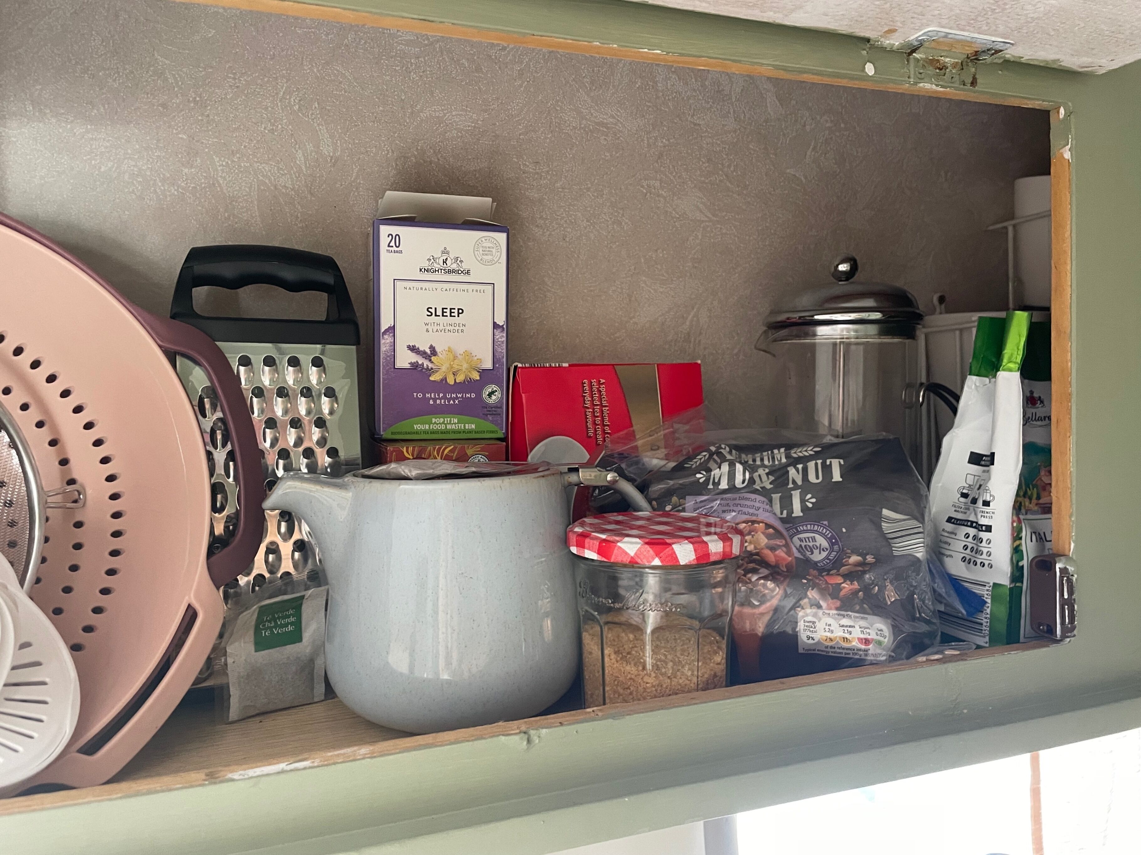 Una despensa con diversos alimentos, incluyendo una caja de bolsitas de té, un tarro de nueces y un colador.