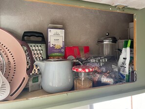 A pantry with various food items, including a box of tea bags, a jar of nuts, and a colander. - Cosy Caravan Sleeps 2 With Patio and Parking (Kilteean)