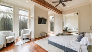 A bedroom with a large bed, two armchairs, a TV, and a ceiling fan.