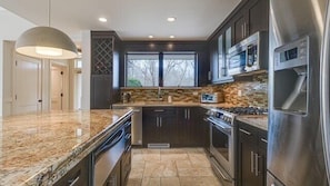 A modern kitchen with granite countertops, stainless steel appliances, and dark cabinetry.