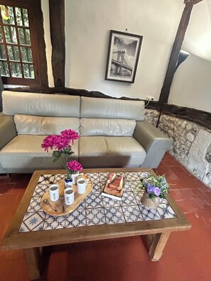 Ein Wohnzimmer mit einem beigefarbenen Sofa, einem Couchtisch mit Tablett, Tassen und Blumen sowie einem gerahmten Bild an der Wand.