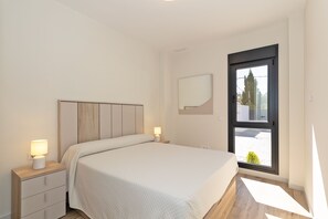 Un dormitorio con una cama, mesitas de noche, una ventana y una puerta.