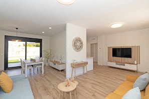 Una sala de estar moderna con comedor, televisor y un amplio ventanal.