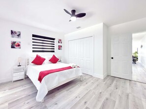 A modern bedroom with a bed, white walls, a ceiling fan, and a door leading to another room. - Gorgeous 2-bedroom house with AC in vibrant Miami (Miami)