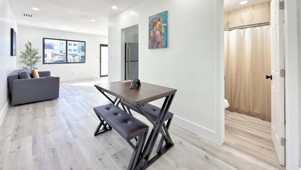 Una sala moderna con un sofá, una mesa de comedor con bancos, un ventanal grande y un cuadro en la pared.