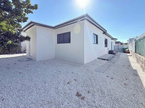 A modern single-story building with a gravel driveway, a small porch, and a green fence. - Gorgeous 2-bedroom house with AC in vibrant Miami (Miami)