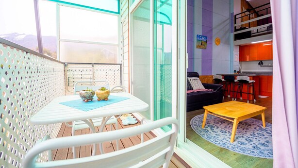 A balcony with a table and chairs, a sofa, and a kitchen area with a bunk bed. - Supia Pension (Pyeongchang)