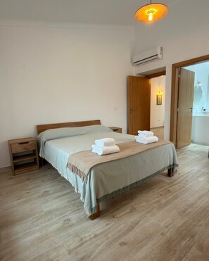Ein Schlafzimmer mit einem Bett, Nachttischen, Holzboden, einer Klimaanlage und einer Tür zu einem Badezimmer.