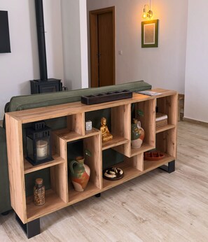 Ein Holzkonsolentisch mit mehreren Fächern, ein grünes Sofa, eine Wandleuchte und eine Tür im Hintergrund.