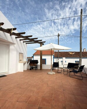 Eine Terrasse im Freien mit Grill, Tisch und Stühlen sowie einem großen Sonnenschirm.