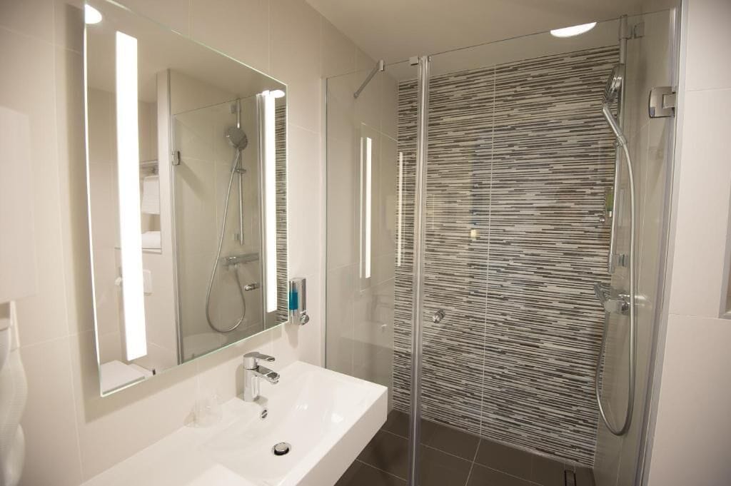 Een moderne badkamer met een glazen douchecabine, een grote spiegel en een witte wasbak.