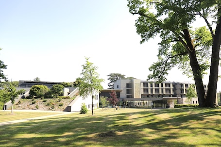 A modern building with a flat roof, surrounded by a grassy area with trees.. MAUBREUIL SEMINAIRES