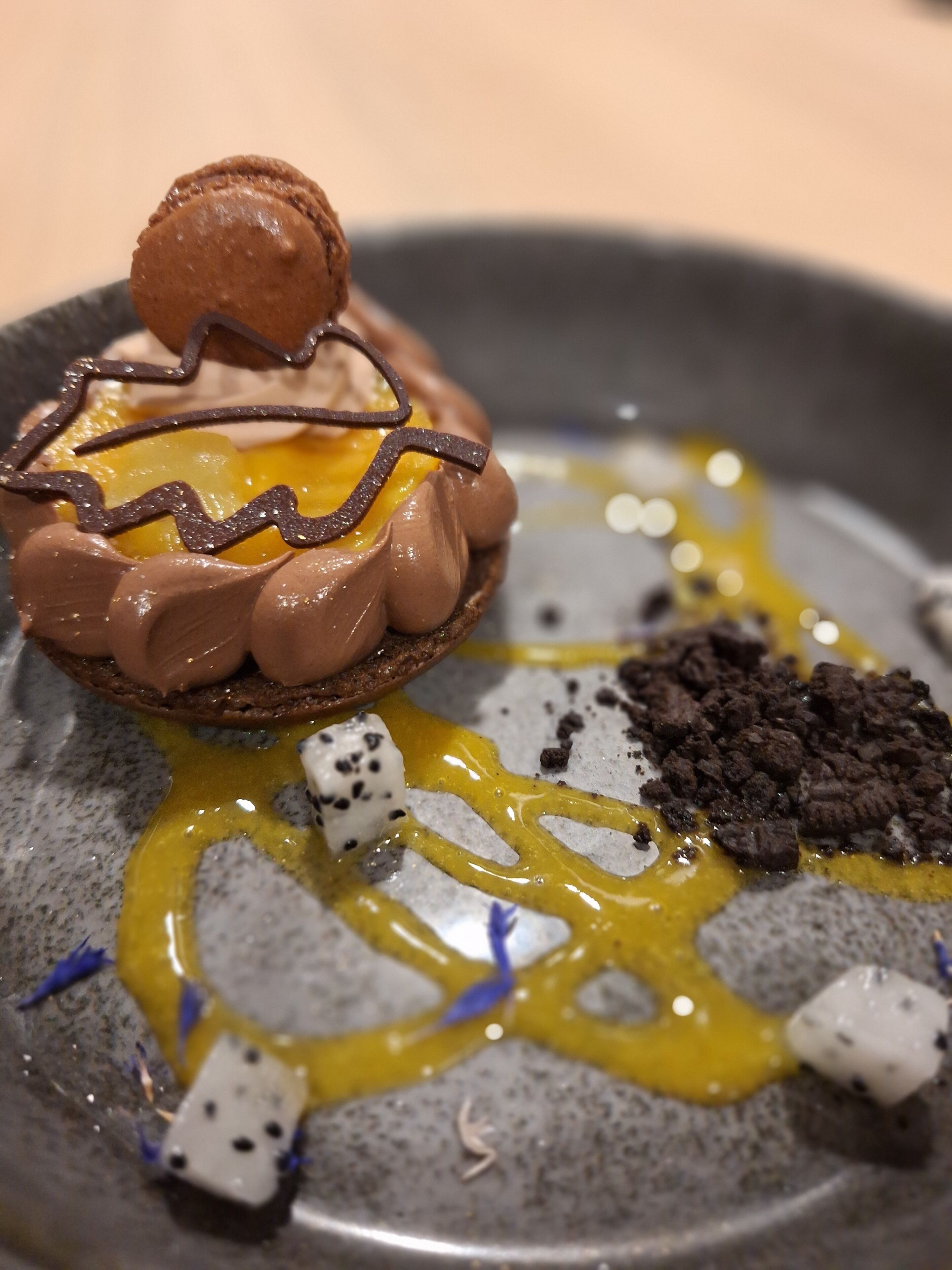 Un dessert au chocolat, agrémenté d’éléments de couleur jaune, présenté dans une assiette.