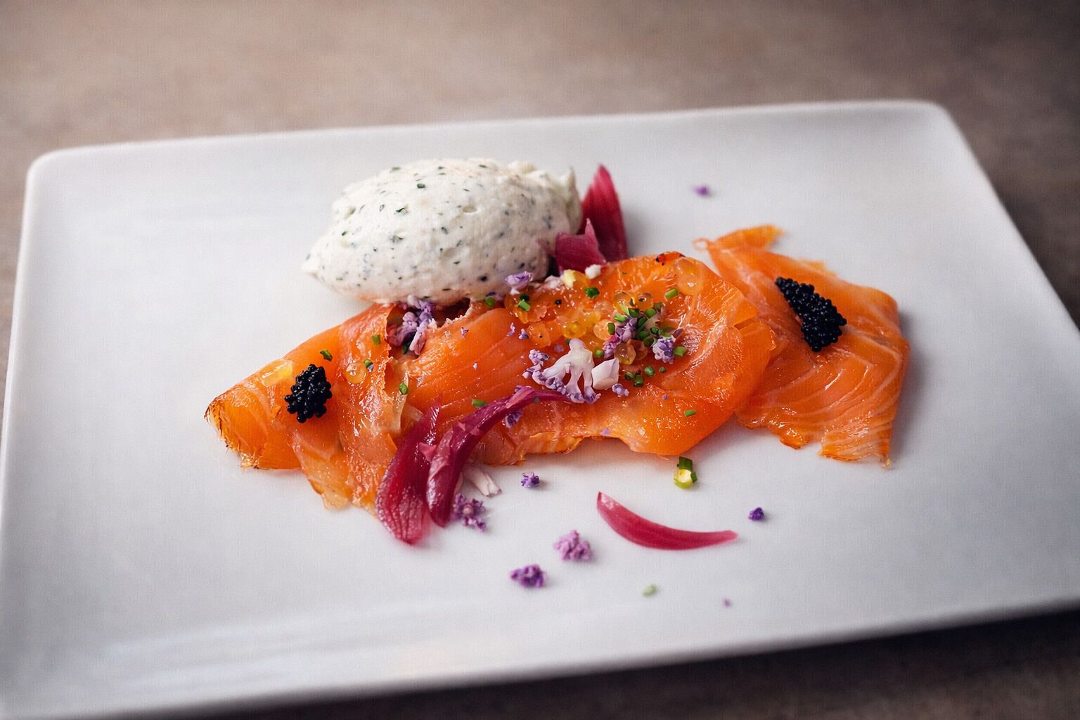 A white rectangular plate with a piece of salmon, red onion, and a dollop of cream.