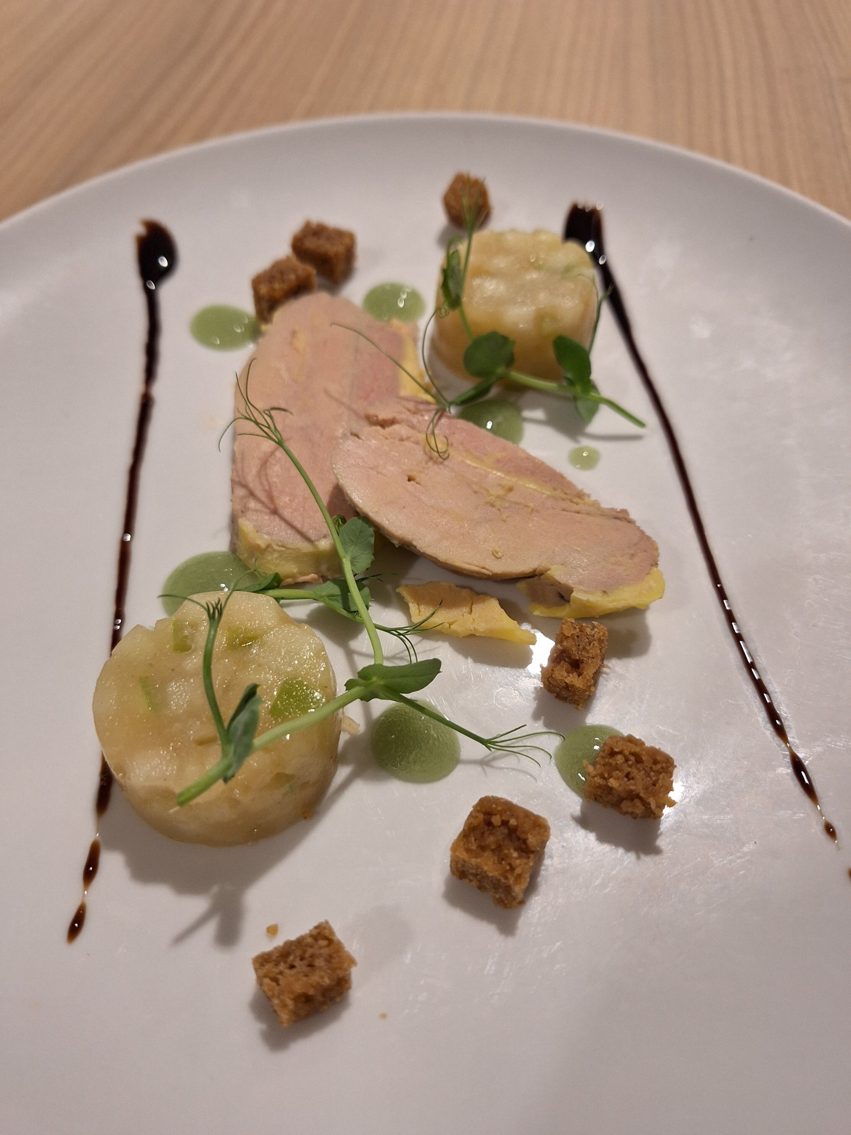 A white plate with food items including slices of meat, green spheres, and croutons.