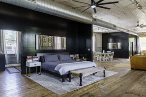 A bedroom with a bed, bedside tables, a desk, and a chair. - Lumberyard Loft in Downtown Brevard (Brevard)