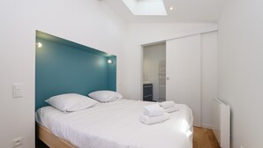 Quarto moderno com claraboia, cama com roupa de cama branca e radiador branco.