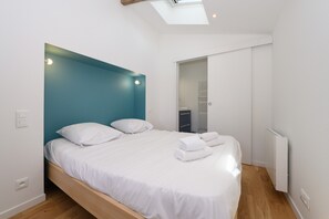 Un dormitorio moderno con tragaluz, una cama con ropa blanca y un radiador blanco.