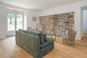 Una sala de estar con una pared de piedra, un sofá verde, una mesa de centro de vidrio y un sillón color crema.
