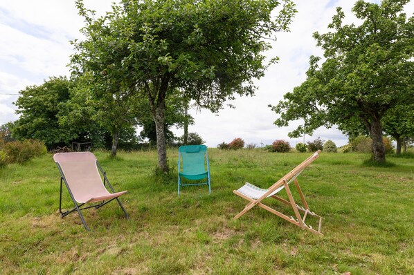 Un entorno al aire libre con dos sillas y un caballete en una zona cubierta de césped y árboles.