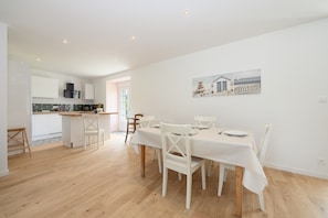 Una cocina moderna con armarios blancos, encimera de madera y una zona de comedor con mesa y sillas blancas.